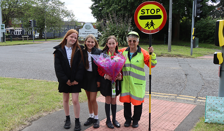 Three pupils give a large bunch of flowers to a school crossing patrol woman