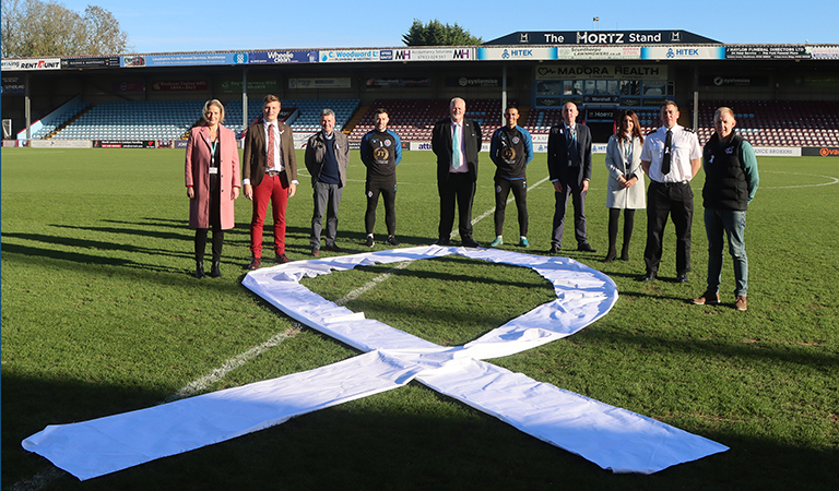 Leader of the council, Rob Waltham pictured at Scunthorpe United grounds and players in support of White Ribbon. They are joined by the Police and Crime Commissioner and the Community Safety Partnership.